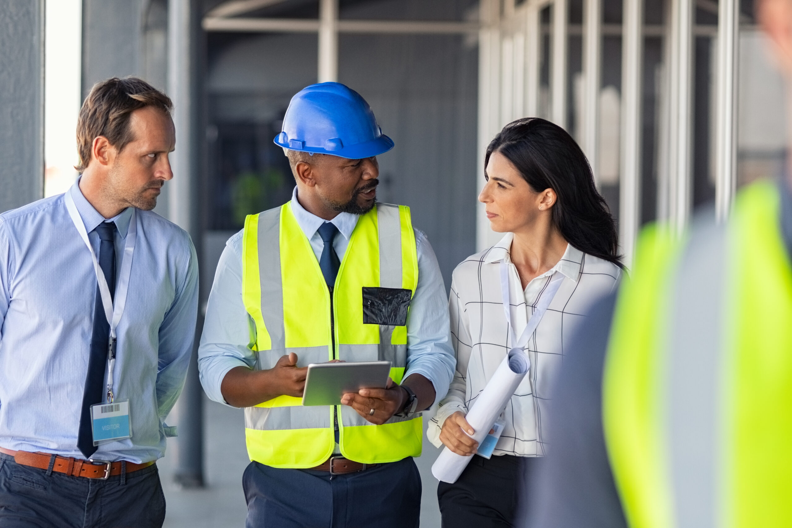 Team of construction workers discussing project details with executive supervisor holding blueprints and digital tablet. Team of architects and civil engineers inspecting construction site. Structural african engineer and architect with work vests discuss the construction process.
